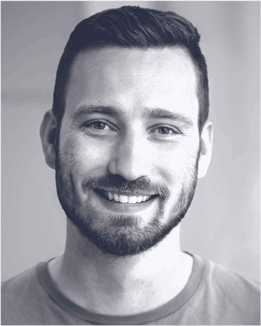 Maik Hummel, head and shoulders, monochrome: short dark hair, a full beard, looking at the camera and smiling.